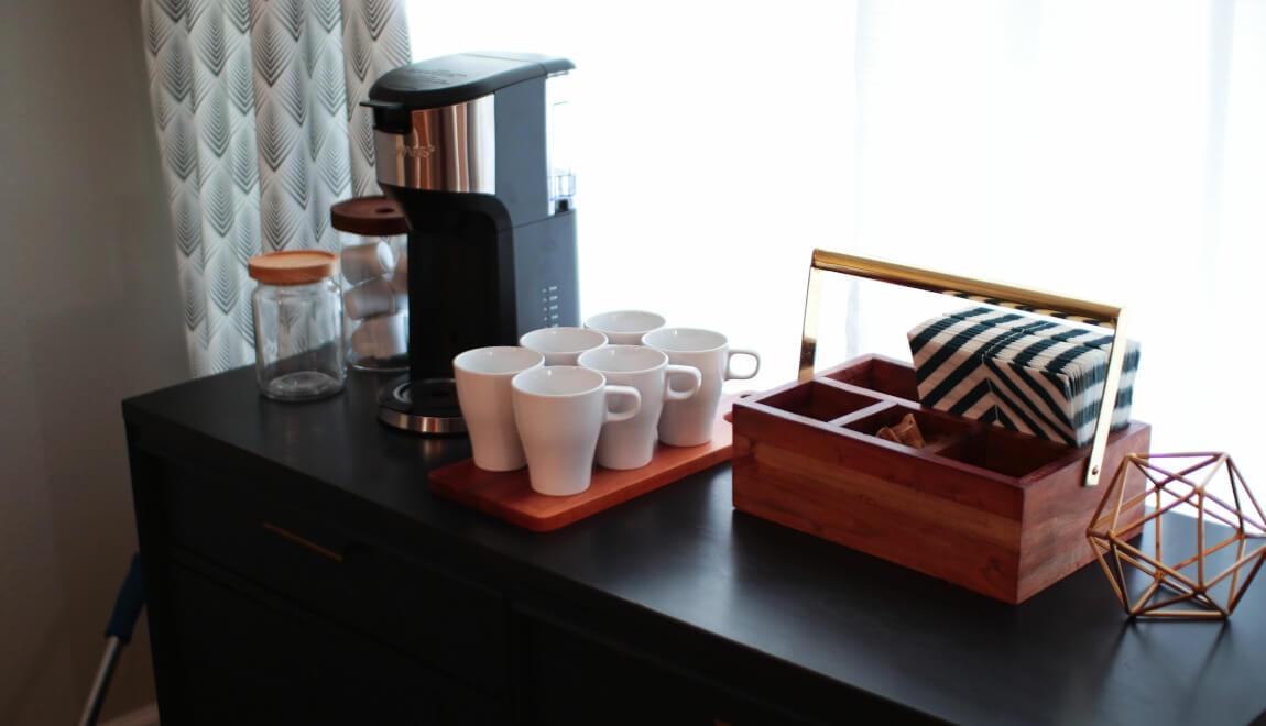 A coffee bar set up near a window featuring a coffee maker, mugs, and some decorations