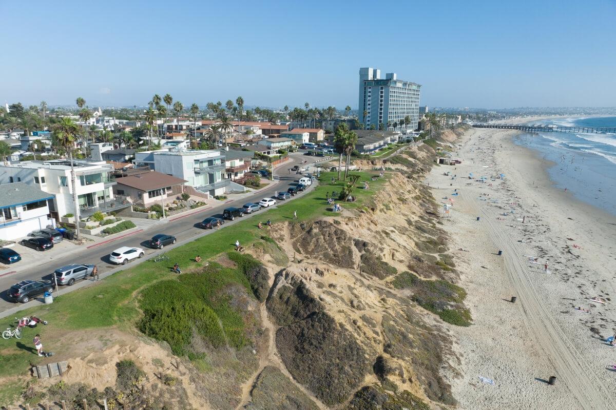 An aerial view of the Pacific Beach coastline shows Crystal Pier in the distance.