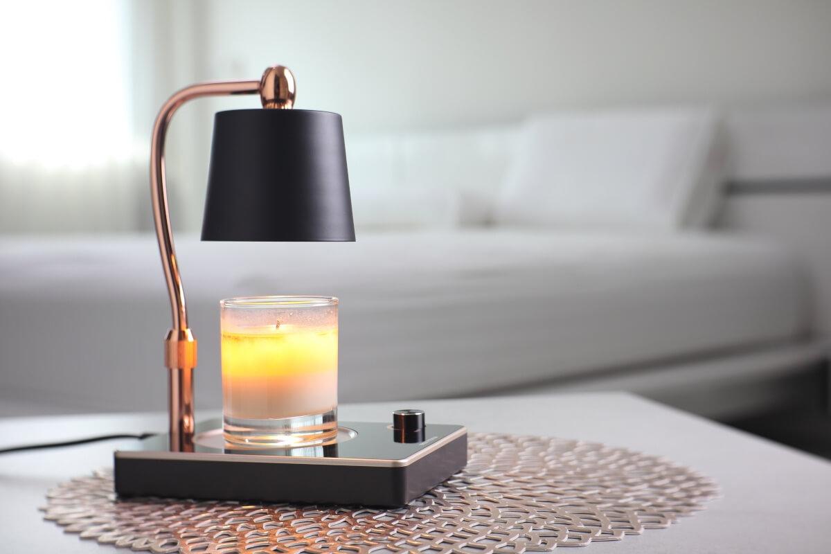 A black candle warmer lamp heats a small candle in an apartment bedroom.