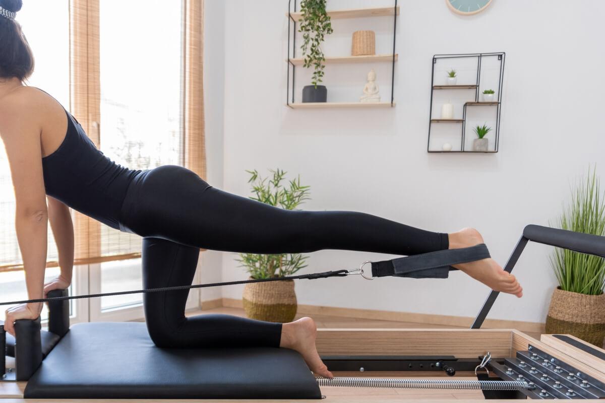A woman does Pilates exercises on a Pilates reformer.