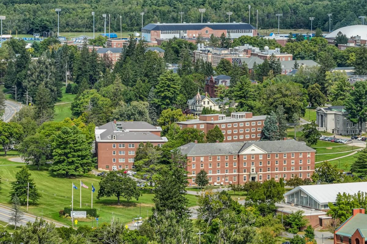 An aerial view of the UMaine campus in Orono shows the college's brick buildings scattered throughout Orono's green grass.