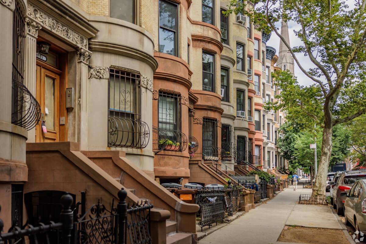 A row of brownstone homes sit along a sidewalk in Brooklyn.