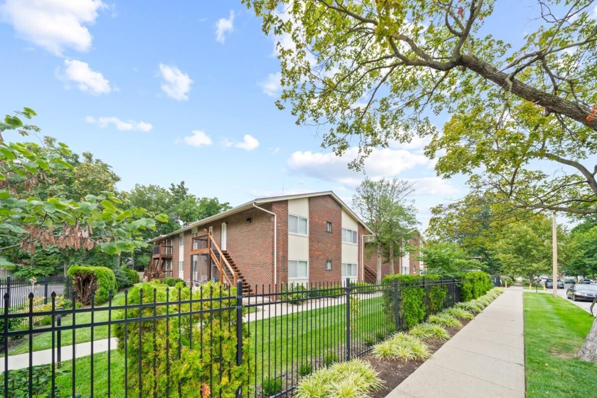 The Charlotte Square apartment community is surrounded by green grass and sidewalks lined with trees.