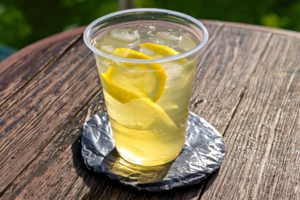 A cup of iced lemon water on a small coaster made from gray plastic grocery bags sits on top of a patio table.