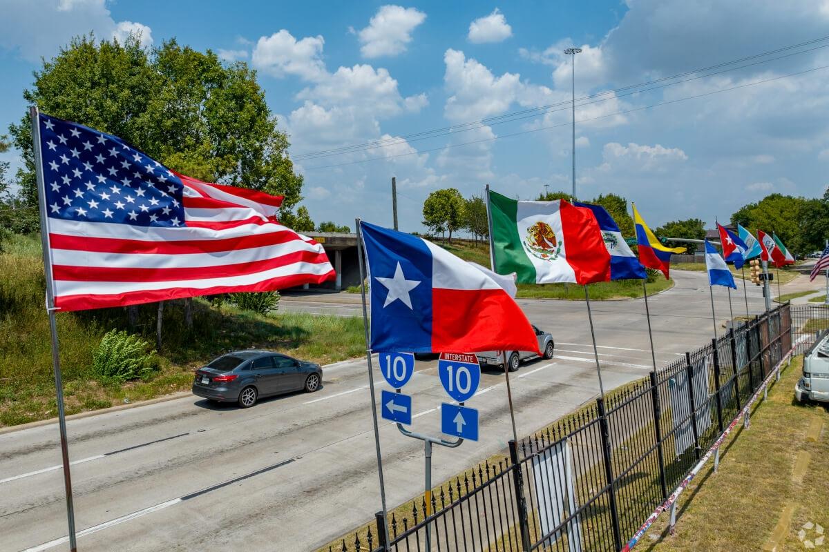 Eight different flags fly behind the American flag and the Lone Star Flag.