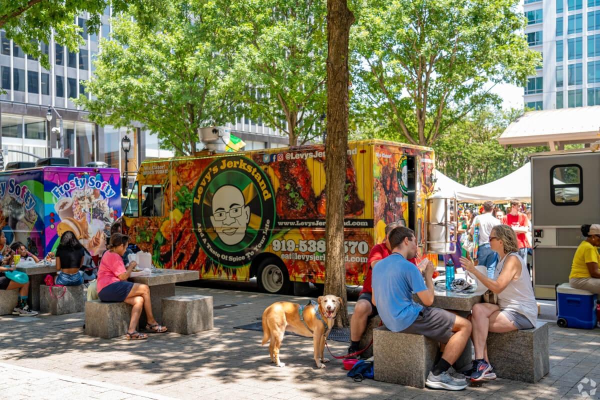 Dog sitting next to people who are eating food from the food truck behind them.