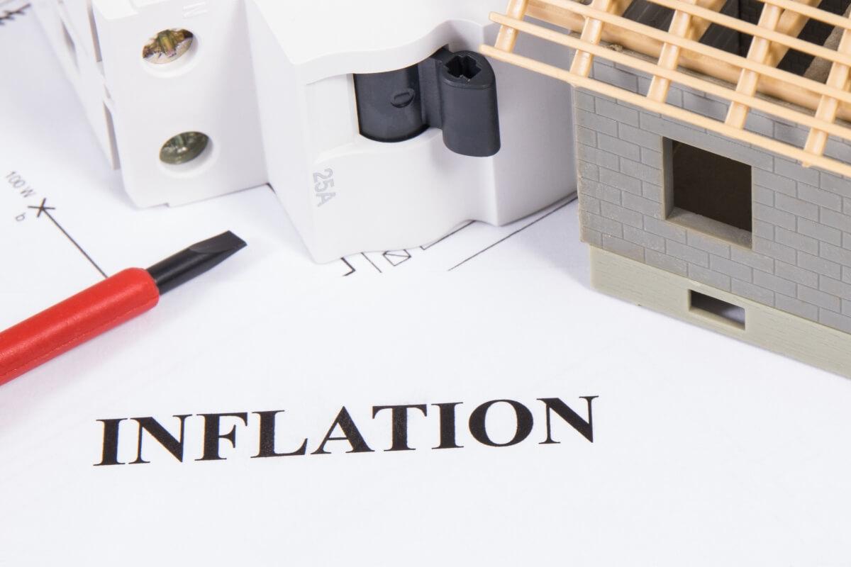 Inflation on a paper underneath a model house surrounded by drafting supplies.