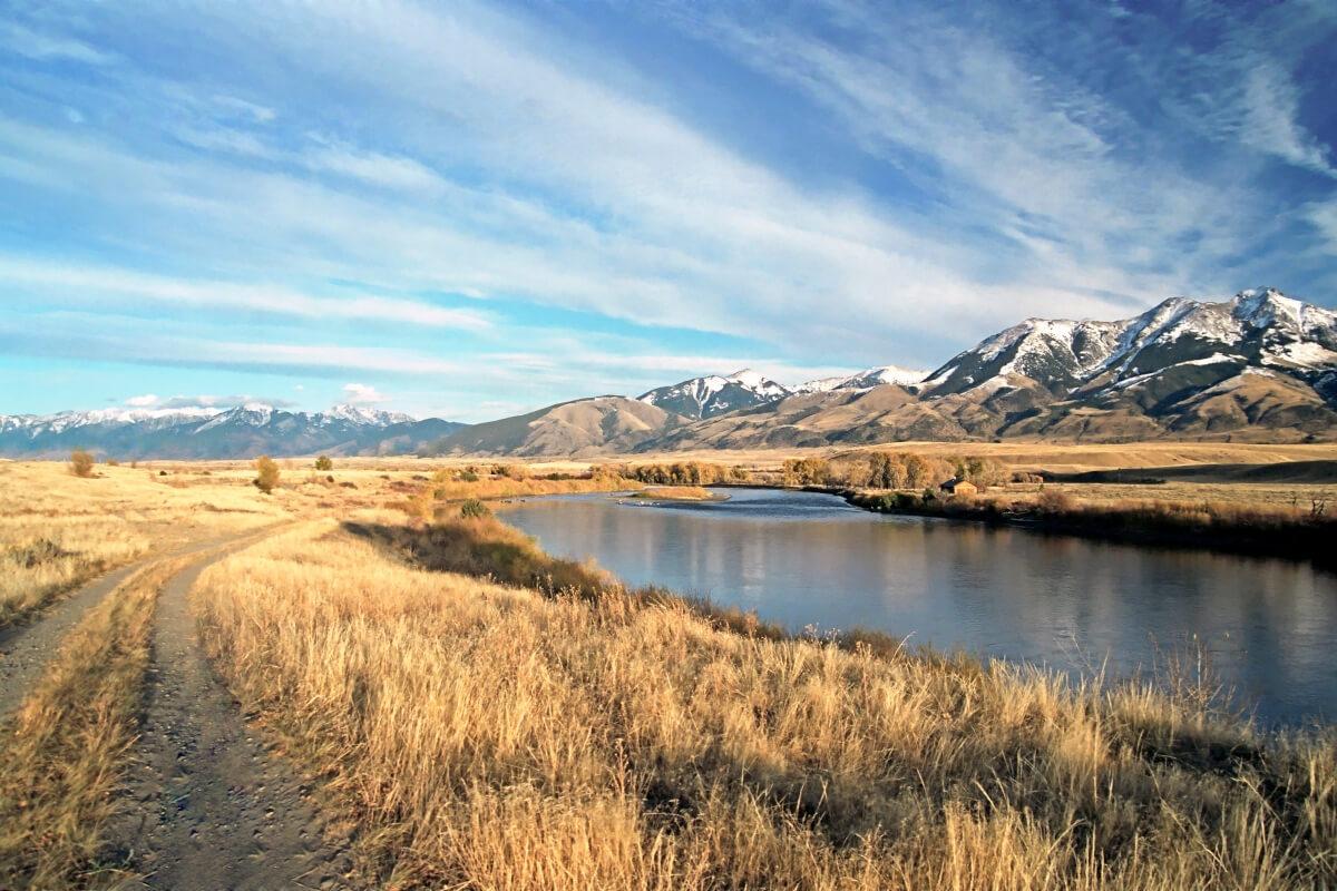 A tranquil river winding through golden grasslands, with snow-capped mountains in the distance under a blue sky.