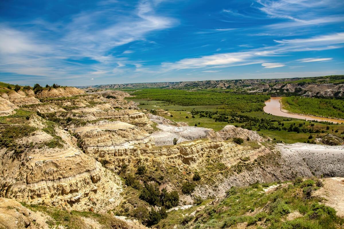Wide view of layered hills, green trees, and a winding river under a blue sky.