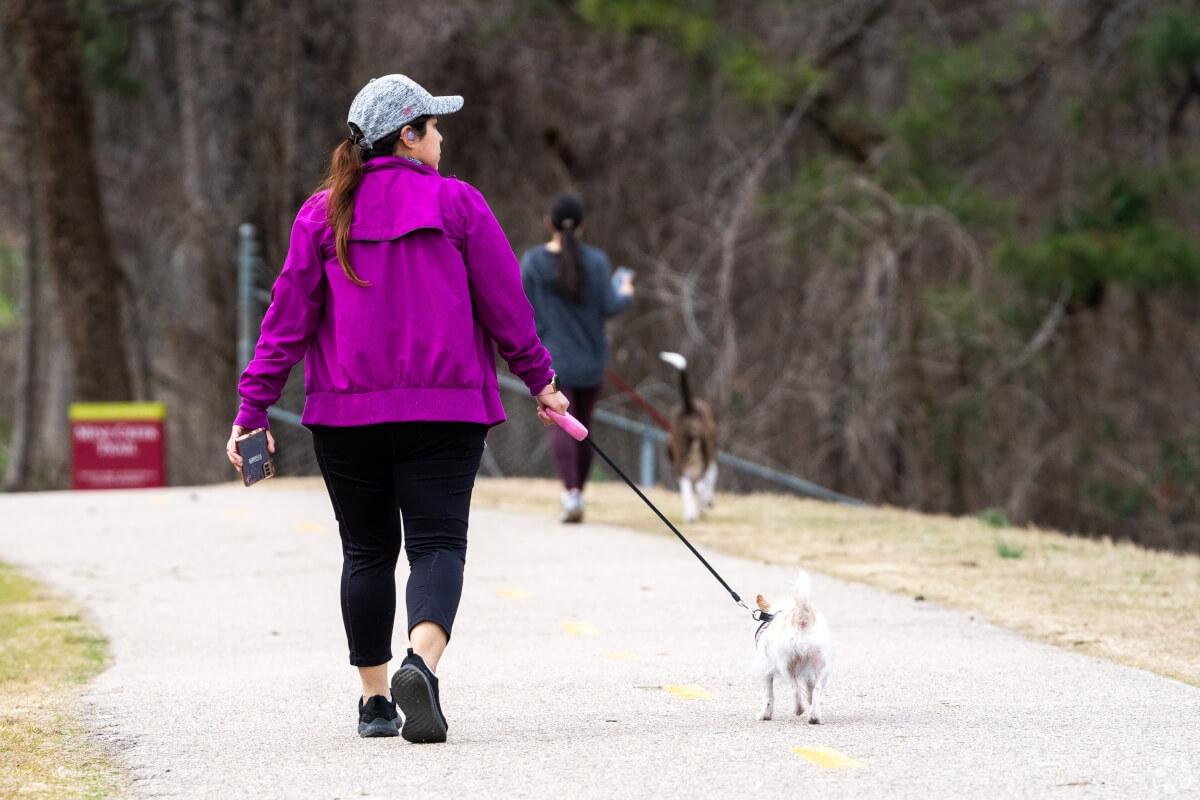 Person walking their small dog on a paved trail.