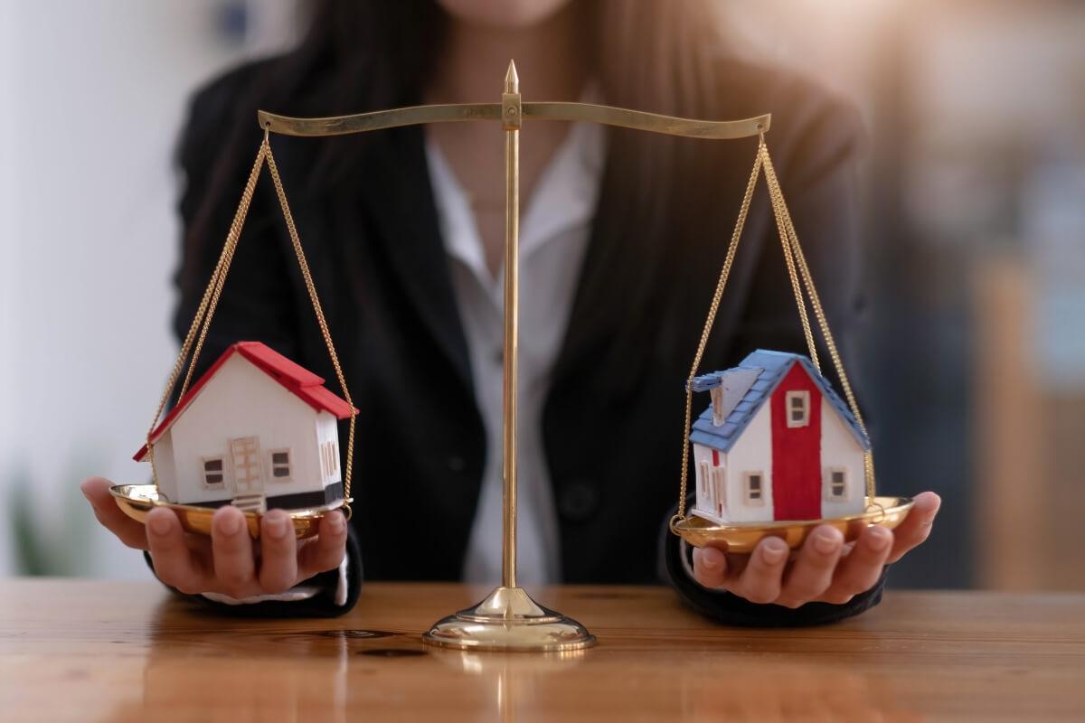 A scale with houses on each side and someone holding them.