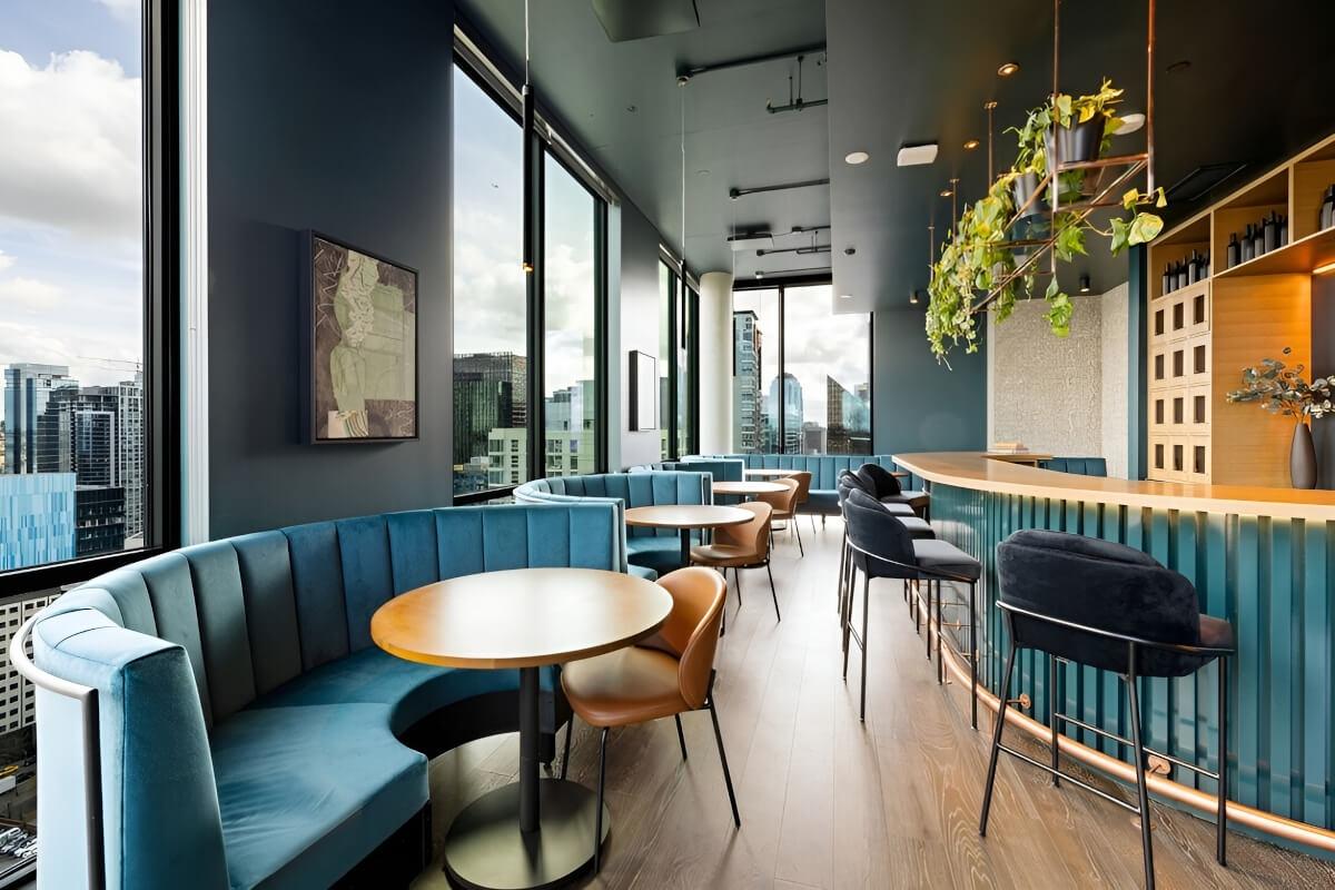 Turquoise couches surround small tables with bar chairs next to a bar in a whisky bar.