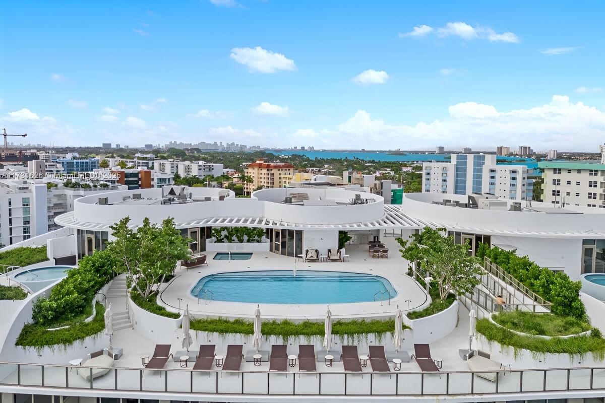 Lounge chairs sit in front of rooftop pool surrounding by greenery in planters.