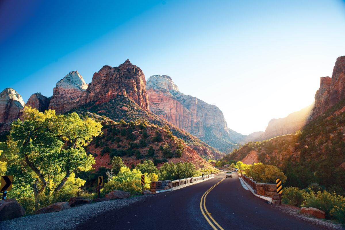 A scenic winding road through Zion National Park with tall red rock mountains and green trees.