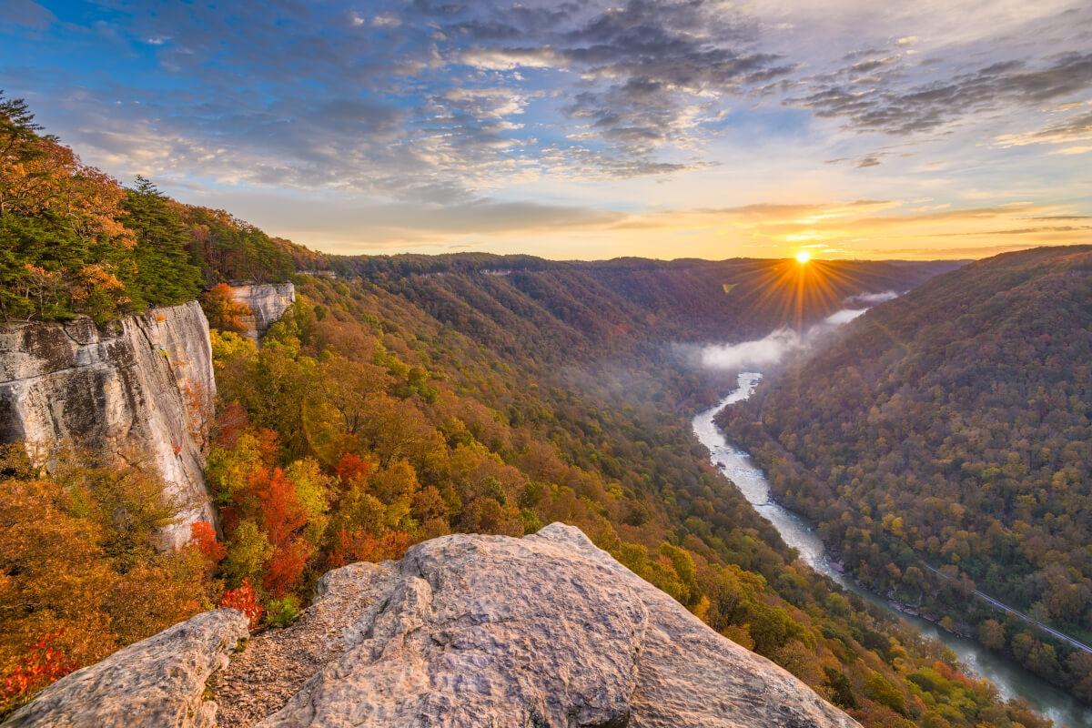 A sunset over a valley with colorful autumn trees and a river winding through it.