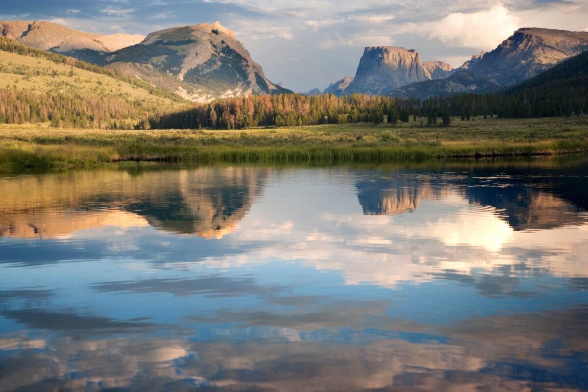 A tranquil lake reflects mountains and a blue sky with clouds.
