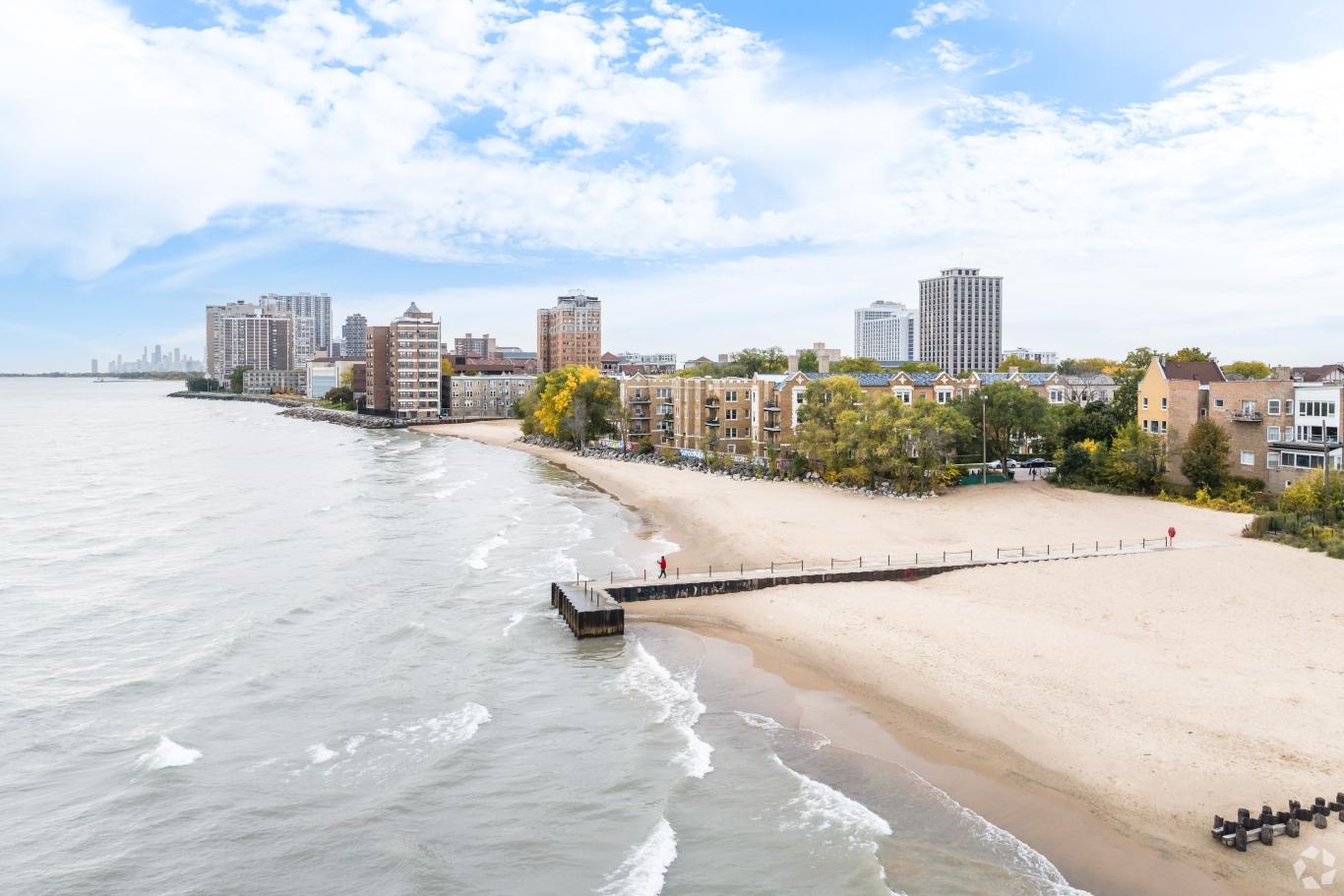 View of Edgewater Beach with people walking along the sandy shore, backed by high-rise apartment buildings in Chicago.