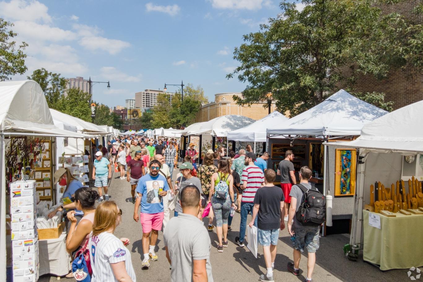 Crowded outdoor art fair in Lakeview with vendor tents and attendees walking through the street on a sunny day.
