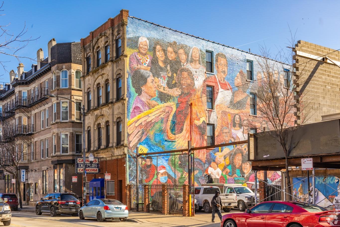 Colorful mural depicting diverse figures on the side of a brick building in the Pilsen neighborhood of Chicago.