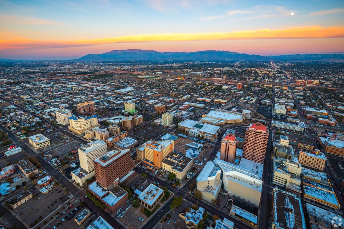 An aerial view of Downtown Albuquerque at sunset with mountains in the distance.