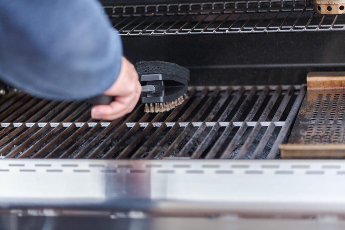 A person uses a grill brush to clean the grates of a grill.