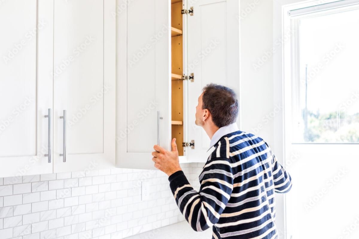Man looking in an empty kitchen cabinet