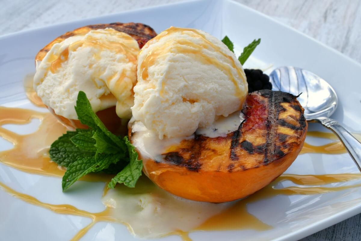 A close-up shot of grilled peaches served with vanilla ice cream and caramel drizzle.