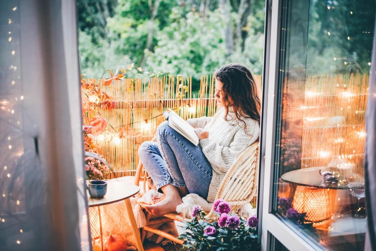 A young woman reads on a porch with string lights.