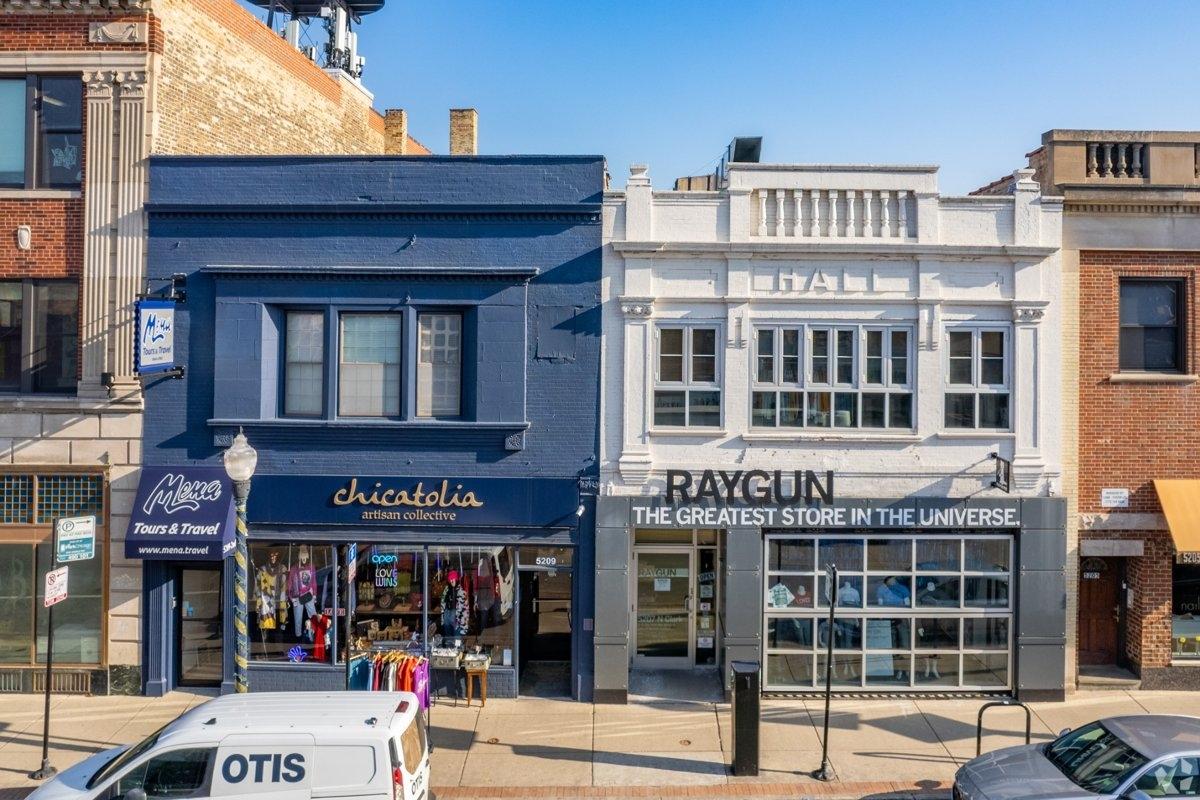 A street-level view of two adjacent storefronts in Andersonville, one painted dark blue reading “Chicatolia artisan collective” and the other white with “Raygun – The Greatest Store in the Universe” signage.