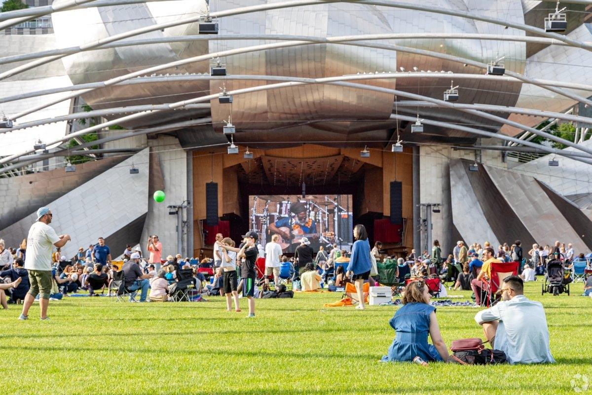 People relaxing and playing on the lawn in front of Jay Pritzker Pavilion during a live outdoor performance.