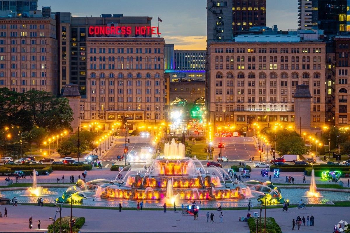 Buckingham Fountain illuminated at dusk in front of the historic Congress Hotel and bustling city traffic.