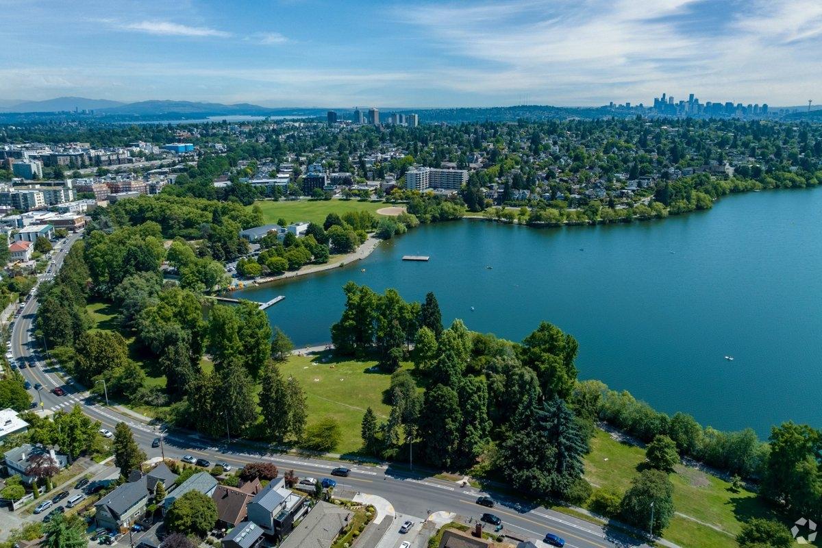 Vibrant aerial view of Green Lake Park in Seattle on a clear summer day, with lush trees, blue lake waters, paddleboarders, and city skyline in the distance.