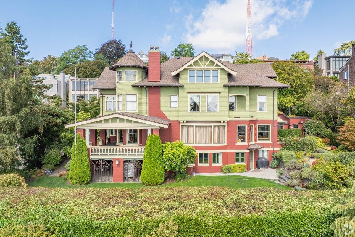 A large, historic Victorian-style house with green and red exterior walls, surrounded by manicured hedges and trees in the Queen Anne neighborhood