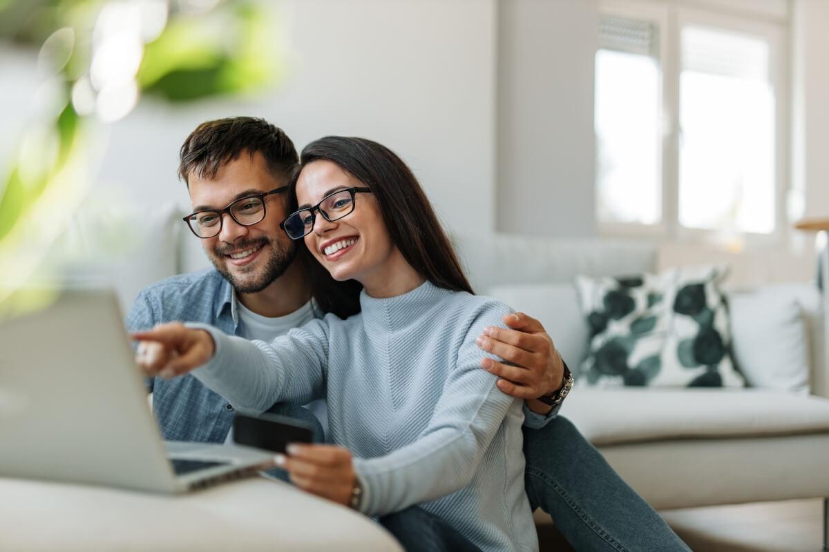 Woman pointing at laptop screen as man sits next to her with his arm around her.
