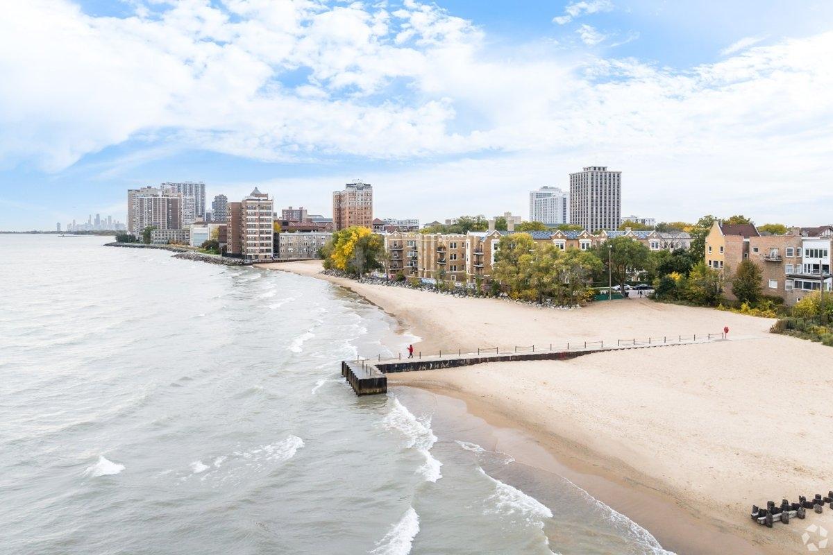 A residential lakeshore in Rogers Park showing brick apartment buildings, a sandy beach, and autumn trees along the water’s edge.