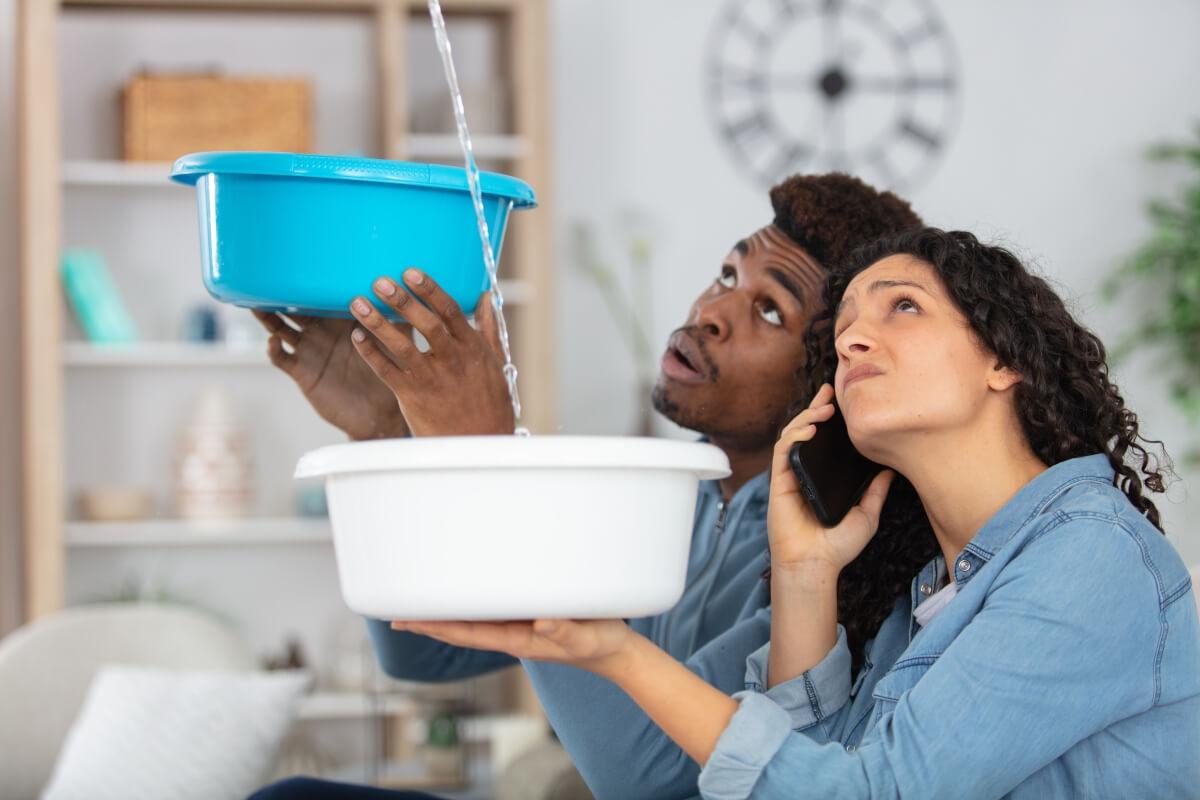 Tenants hold buckets to collect water from apartment leak.