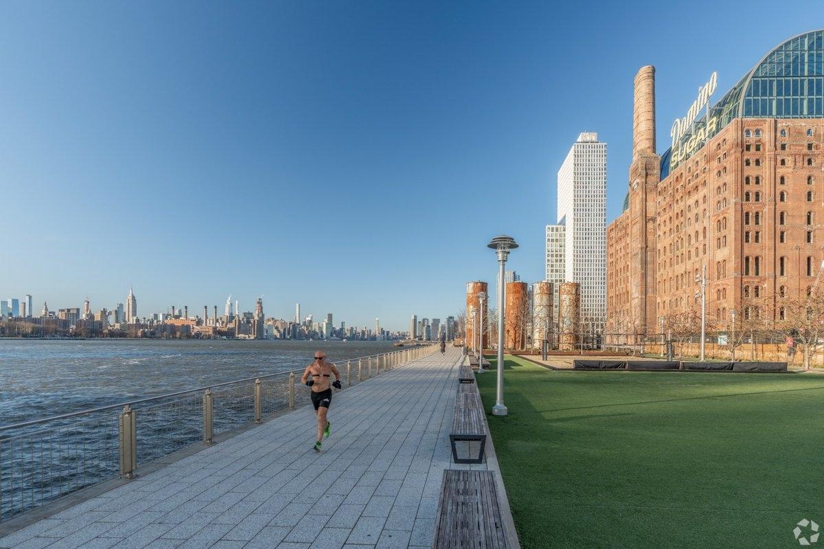 Scenic view of Domino Park along the East River in Williamsburg, with skyline views and walkable green space near modern apartments.