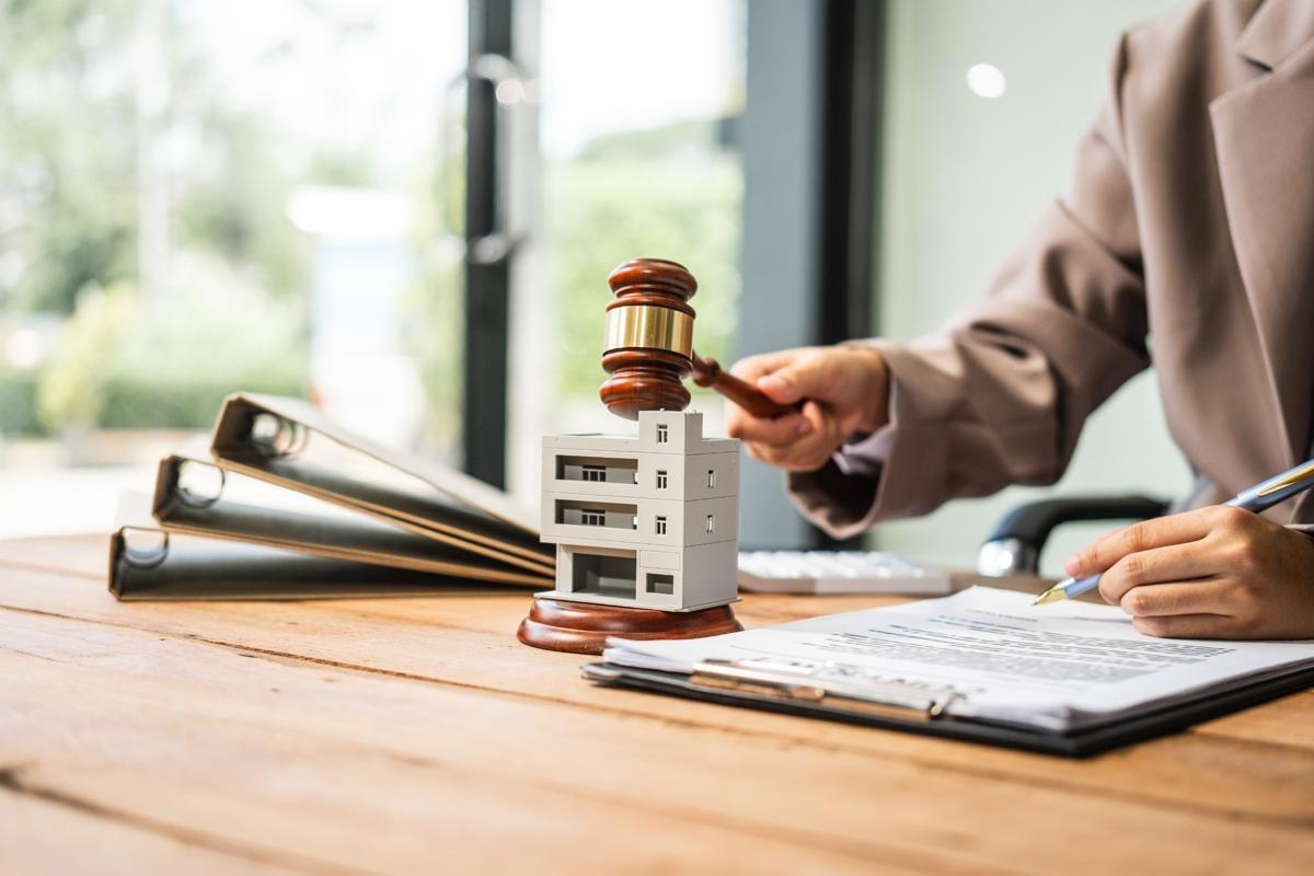 Gavel hitting miniature apartment model next to legal documents, illustrating renters insurance laws and regulations.