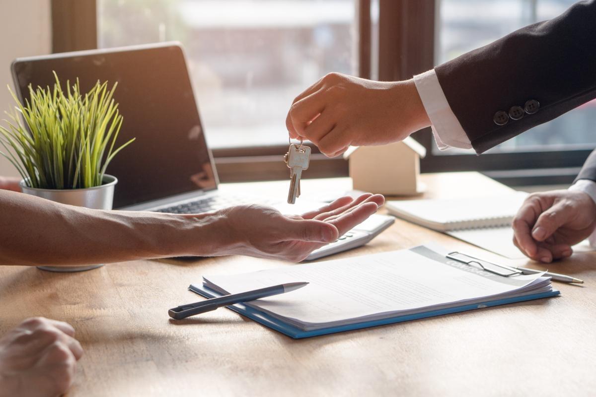 Close-up of a landlord handing apartment keys to a new tenant over a lease agreement, representing the rental process and importance of renters insurance.