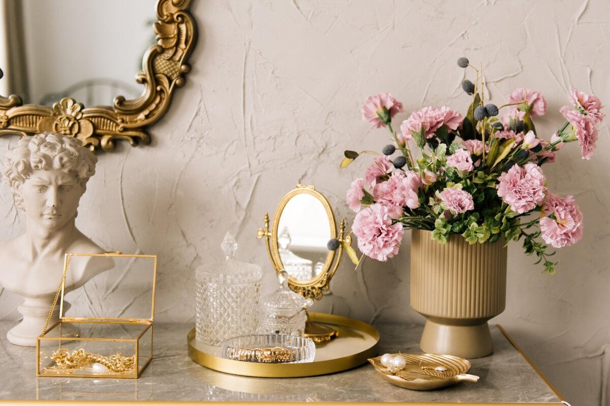 A close-up of a vanity shows a gold vanity tray, gold mirrors, and a small Greek-style bust.