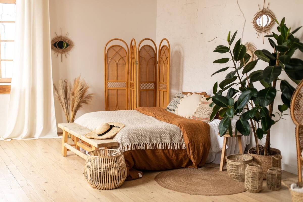 A boho bedroom has a rattan room divider and plants on the ground.