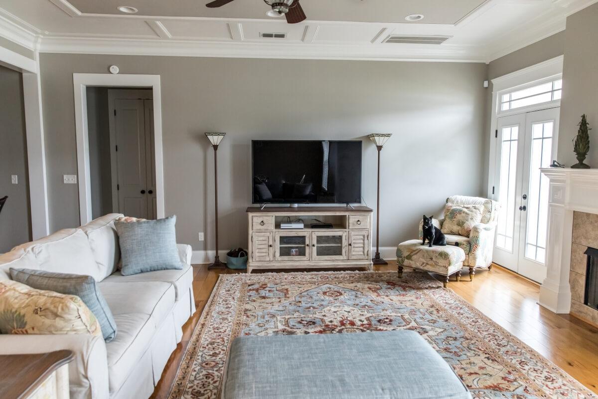 A black cat sits on an ottoman in the corner of a soft transitional living room.