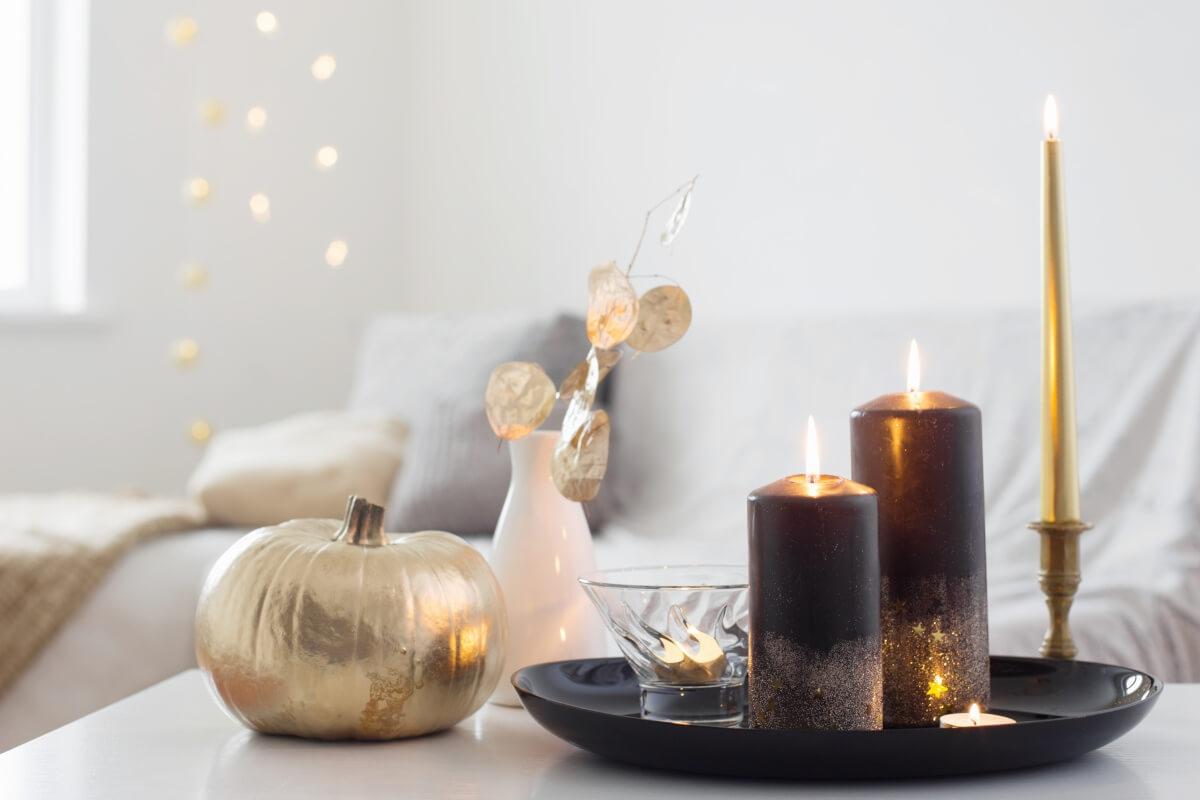 A close-up shot of a gold pumpkin and some lit candles on a white coffee table.