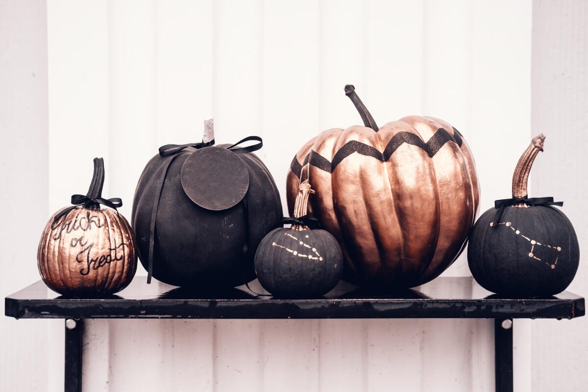 Five black and copper painted pumpkins sit on a black shelf.