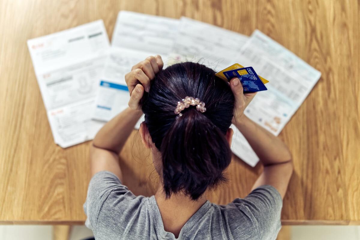 A young woman rests her head in her hands while looking at her credit report and credit card bills.