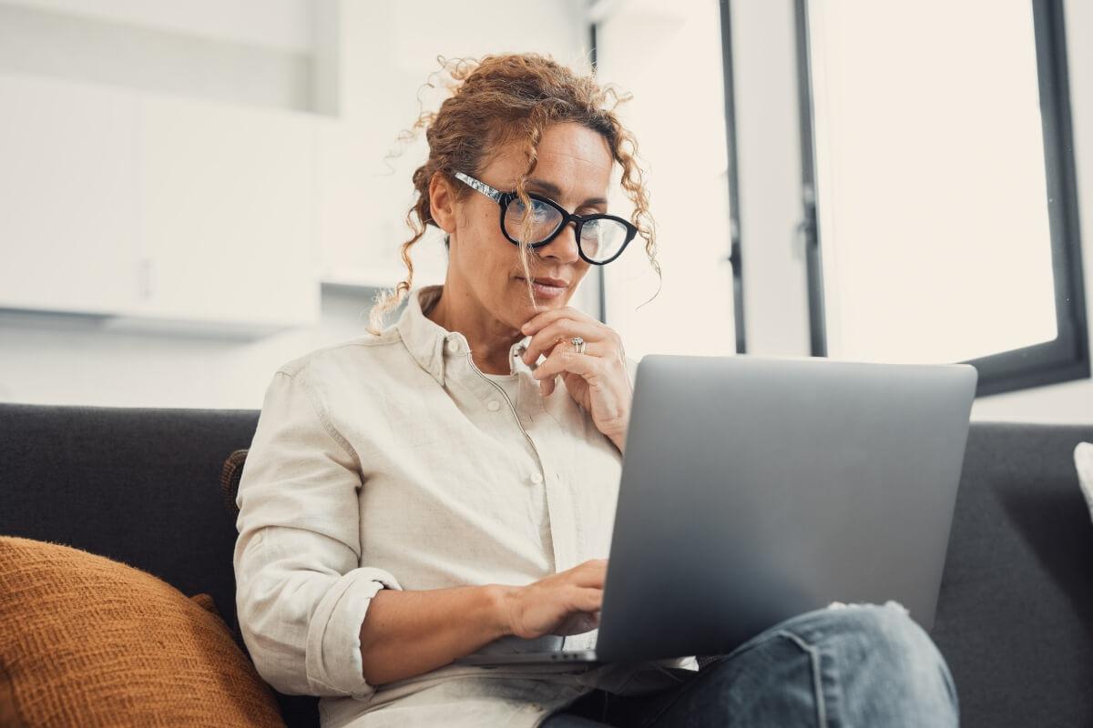 A woman looks thoughtfully at something on her laptop.