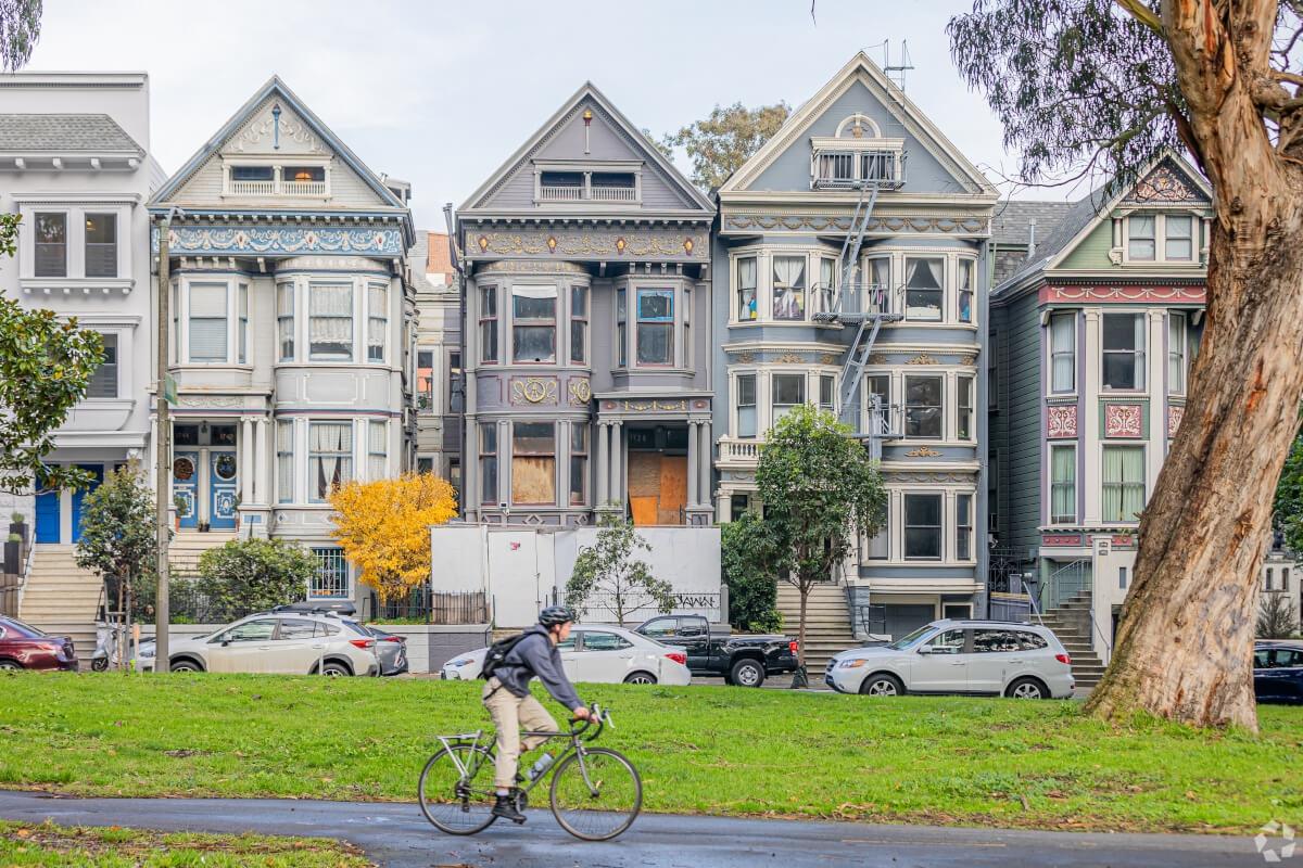 A person rides a bike past colorful Victorian townhomes in San Francisco.