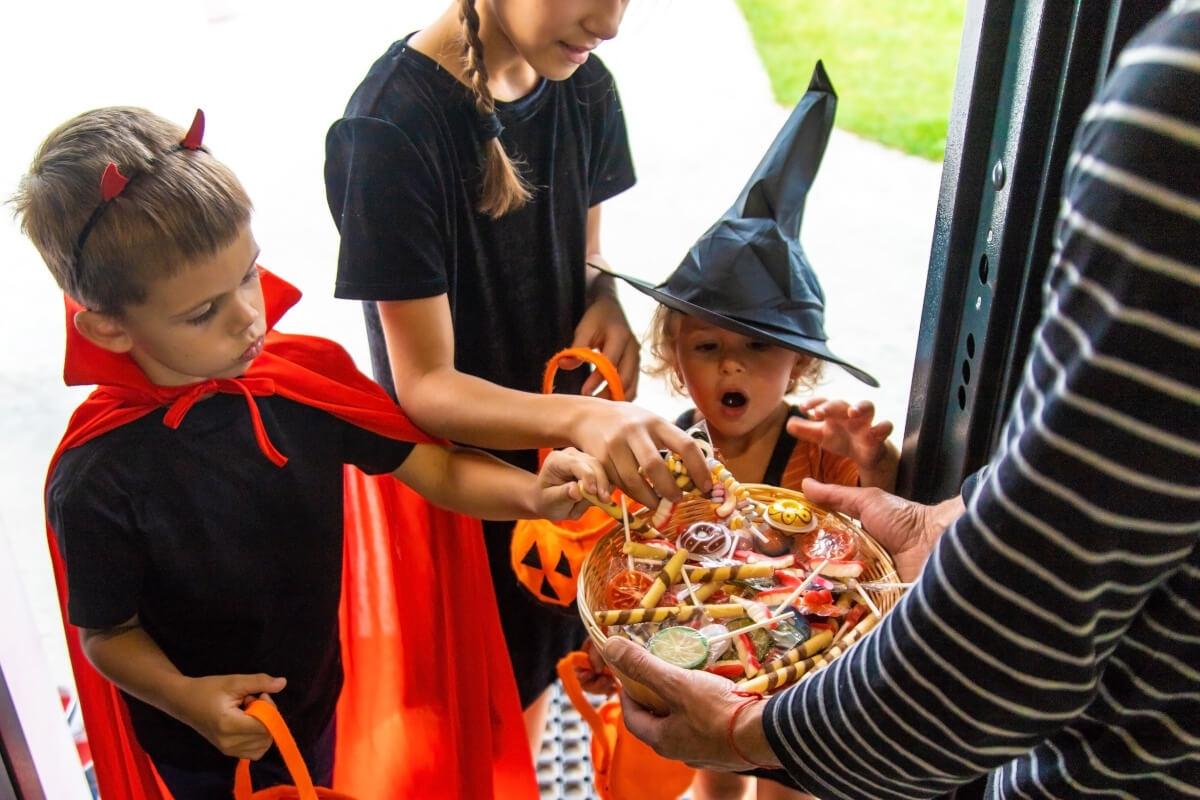 Children in Halloween costumes take candy from a bowl.