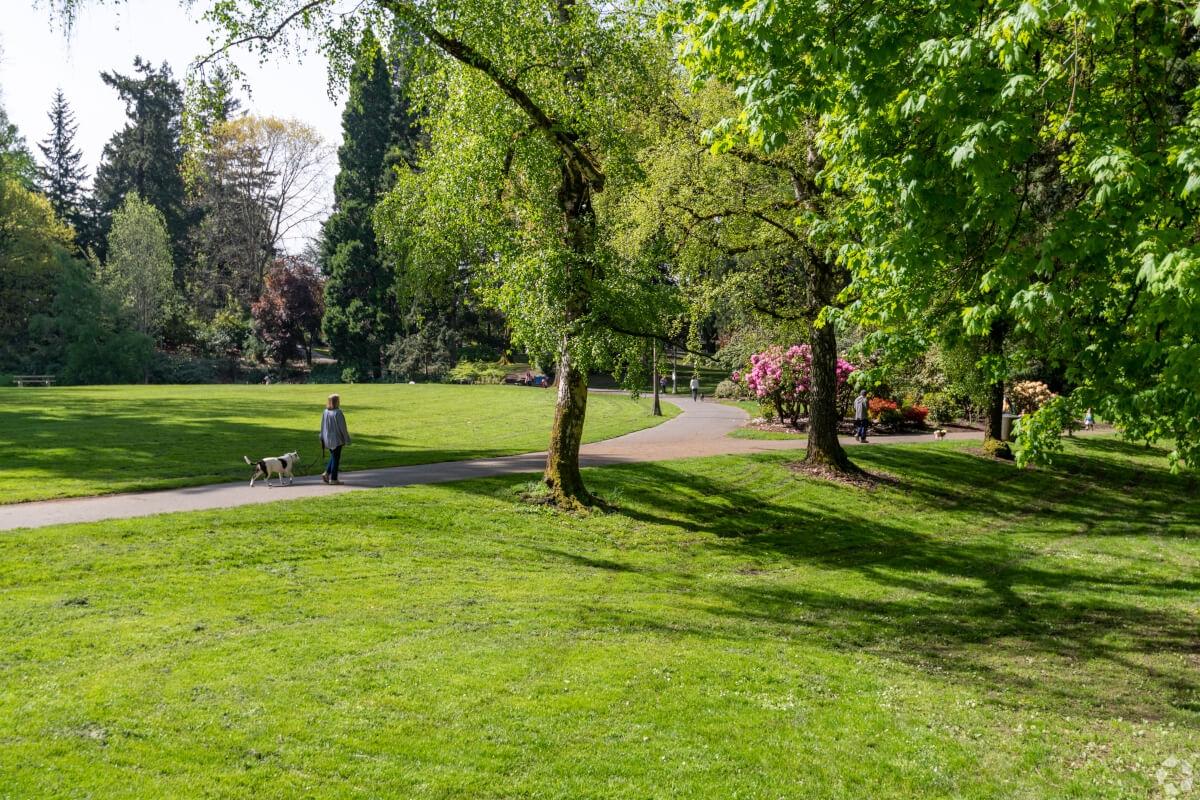 Person walking their dog on a paved trail through Laurelhurst Park.