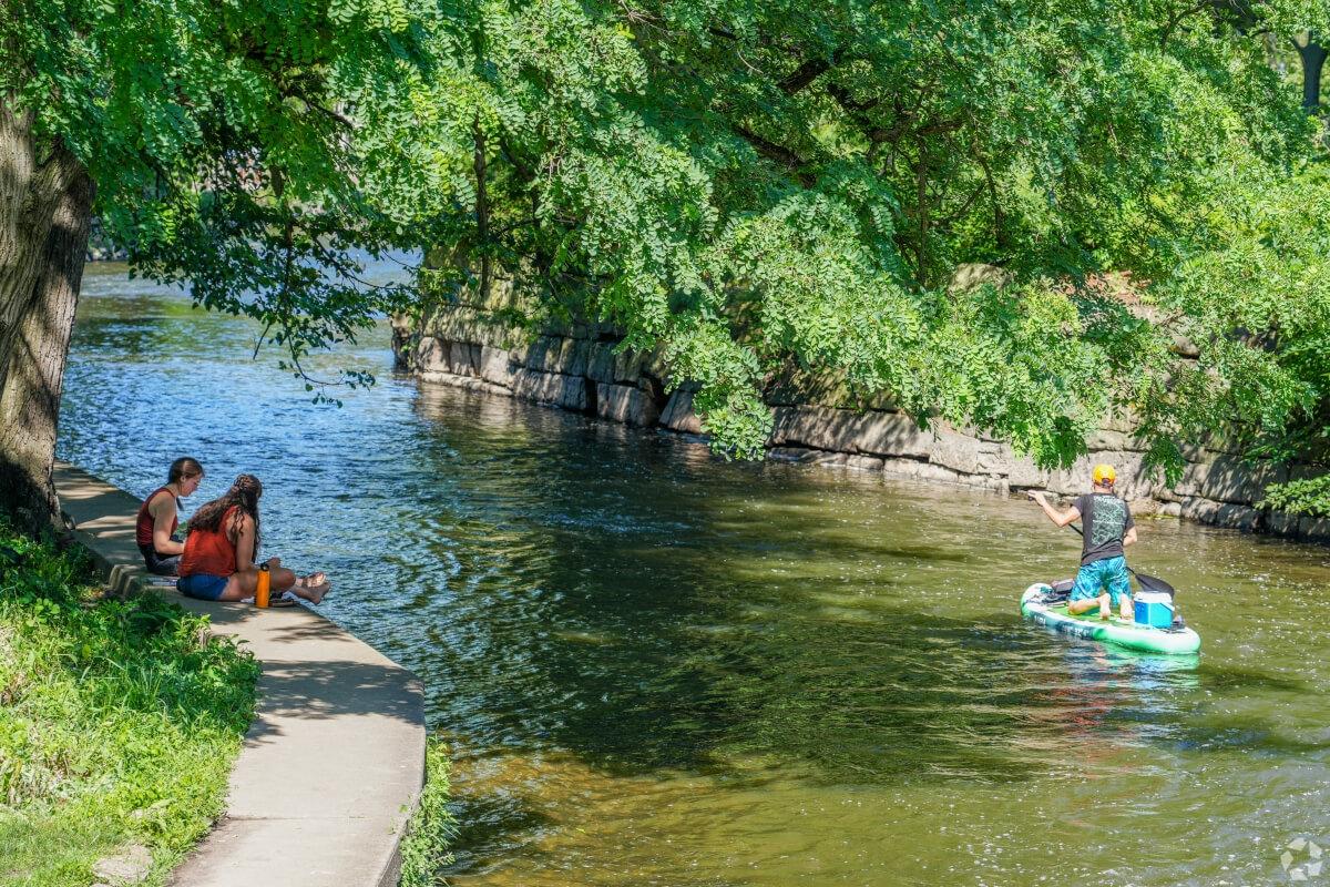 People on the Naperville Riverwalk watch a paddleboarder go by on the DuPage River.